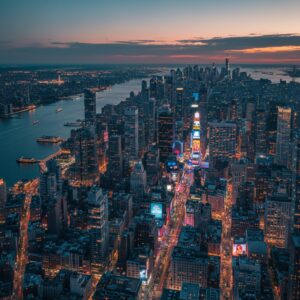 An aerial view of the New York City skyline at dusk with illuminated skyscrapers and the Hudson River.
