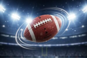 A football spins in mid-air against the backdrop of a brightly lit stadium at night.